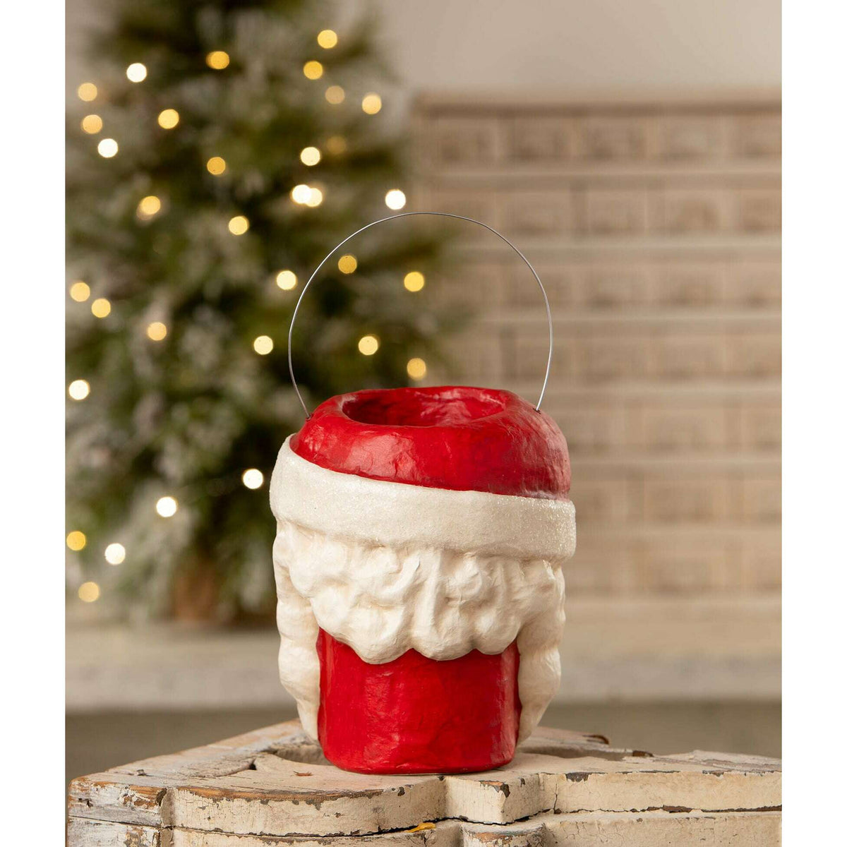 Tall Santa papier-mache Christmas bucket displayed beside a glowing Christmas tree