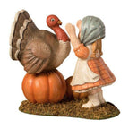 Trudy with Turkey Thanksgiving figurine by Bethany Lowe Designs, showing a little girl in a bonnet and apron reaching up to hug a turkey standing on a pumpkin.