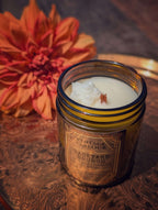 Vintage Parlour Backyard Brunch wooden wick candle in an amber glass jar beside an orange flower on an ornate vintage-style surface