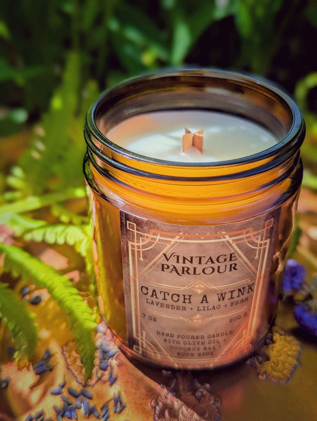 Vintage Parlour Catch a Wink lavender wooden wick candle in an amber glass jar surrounded by greenery