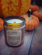 Vintage Parlour Cozy by the Cobblestone wooden wick candle in an amber glass jar displayed on rustic wood with pumpkins in the background
