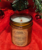 Vintage Parlour Eskimo Kiss wooden wick candle in an amber glass jar displayed with red fabric, evergreen branches and holiday ornaments