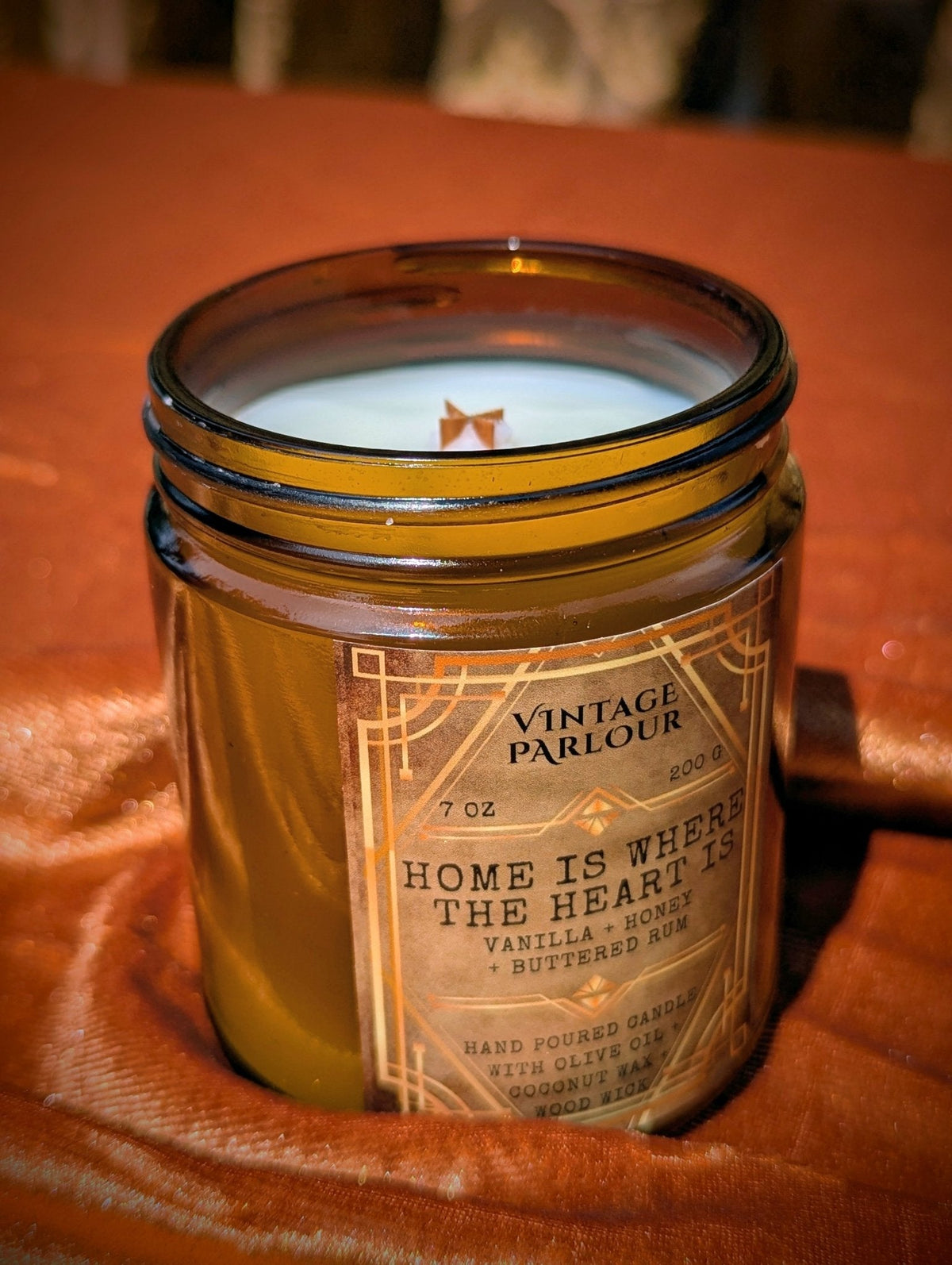 Vintage Parlour Home Is Where the Heart Is wooden wick candle in an amber glass jar nestled in warm copper-colored fabric