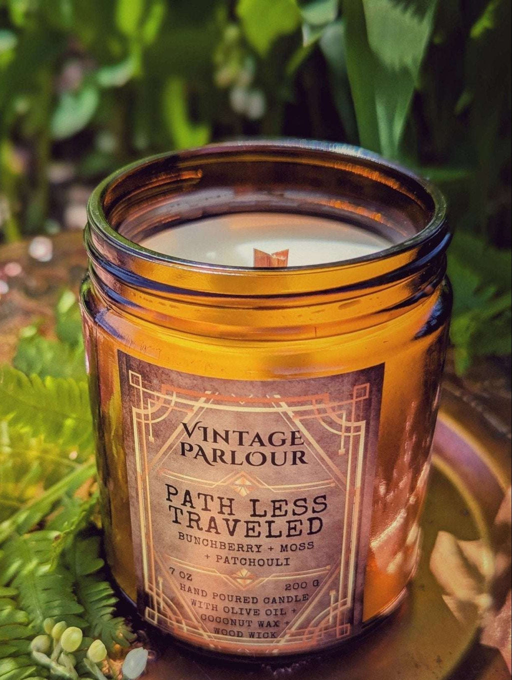 Vintage Parlour Path Less Traveled wooden wick candle in an amber glass jar surrounded by greenery