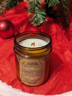 Vintage Parlour Tinsel Tree wooden wick candle in an amber glass jar displayed on red holiday fabric with evergreen branches and Christmas ornaments